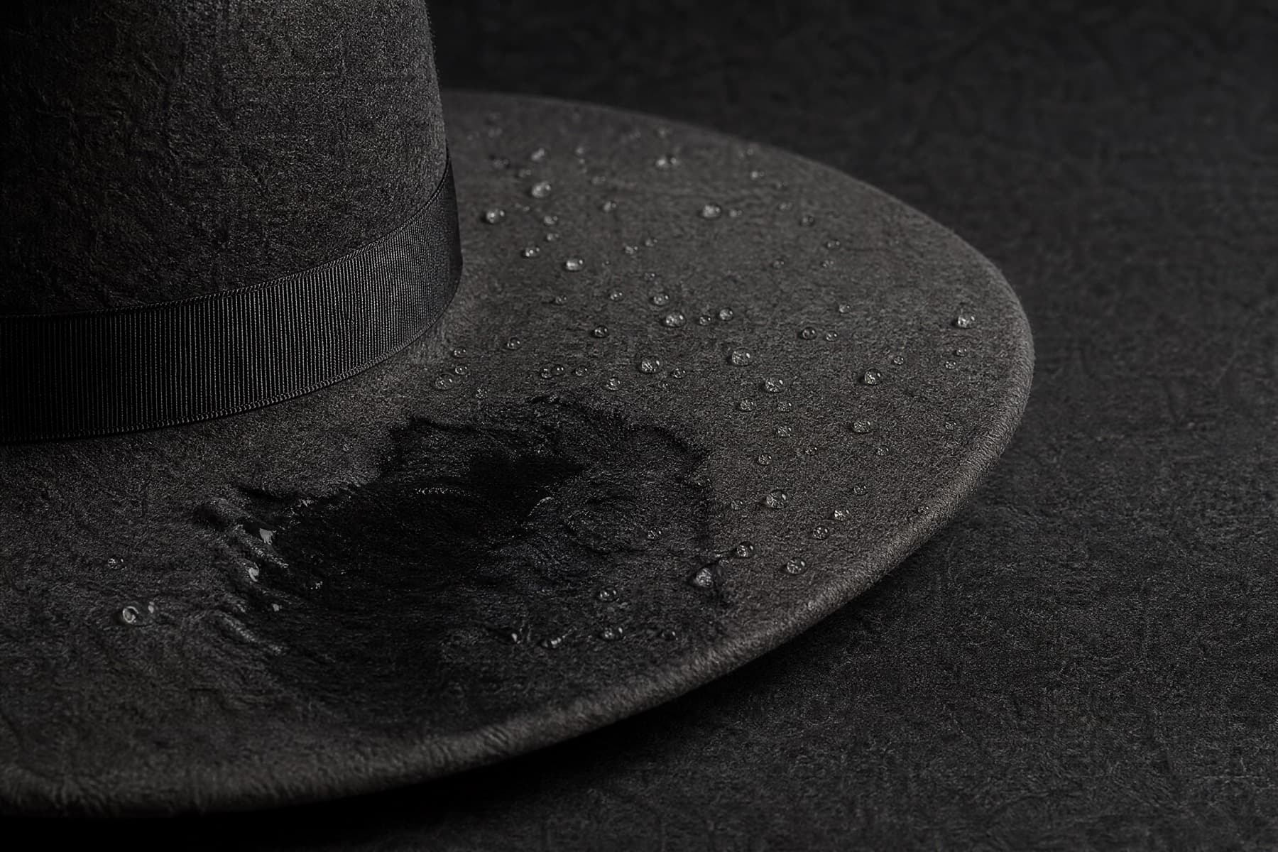 Charcoal felt brim with water beaded on the surface and one area soaked to a darker patch