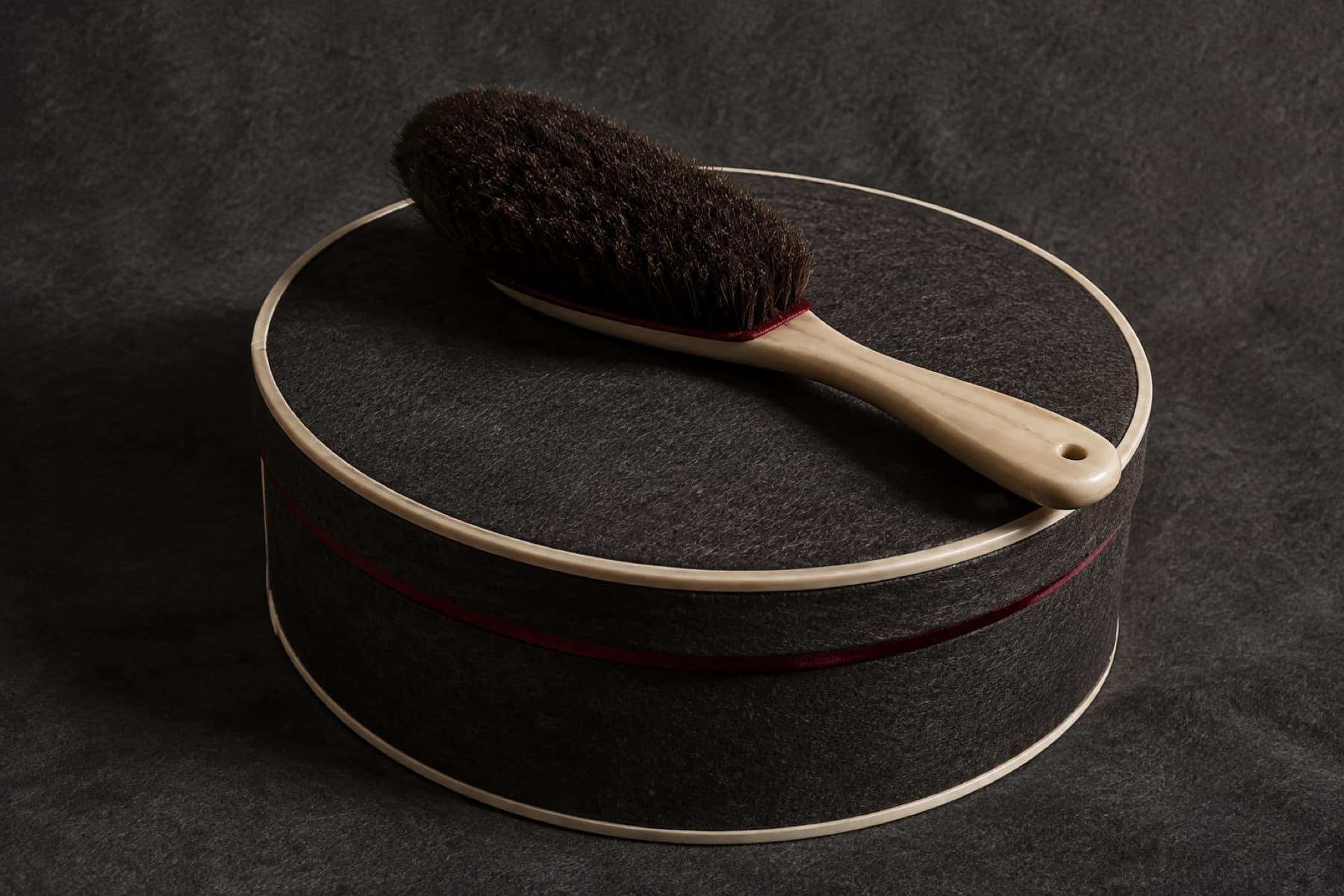 Bone-handled hat brush resting on the lid of a rigid charcoal hat box